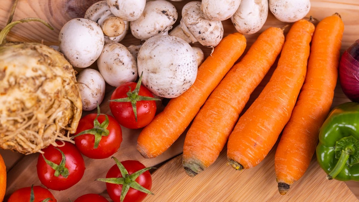 A variety of fresh organic vegetables including carrots and mushrooms on a wooden table.