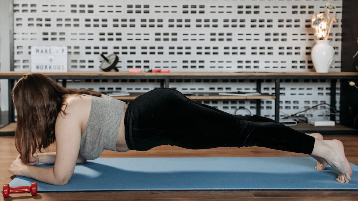 A woman doing plank exercise indoors on a blue mat, promoting fitness and healthy lifestyle.