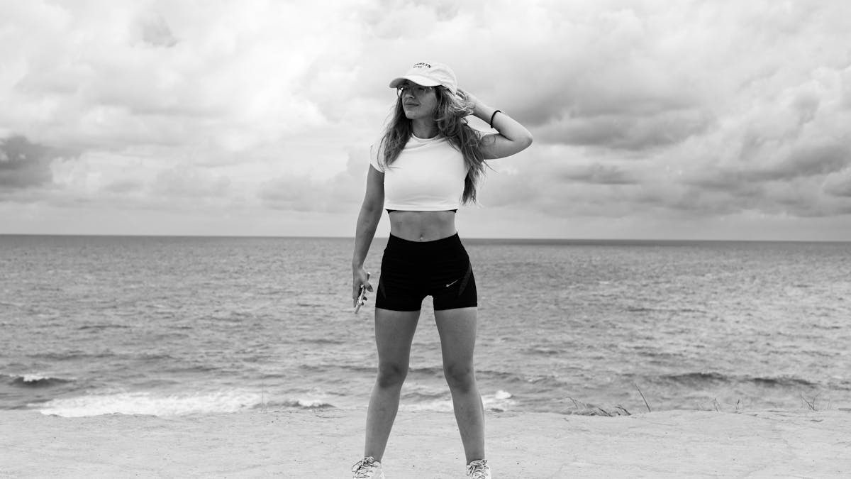 A woman in athletic attire poses near the ocean with a dramatic sky in Natal, Brazil.